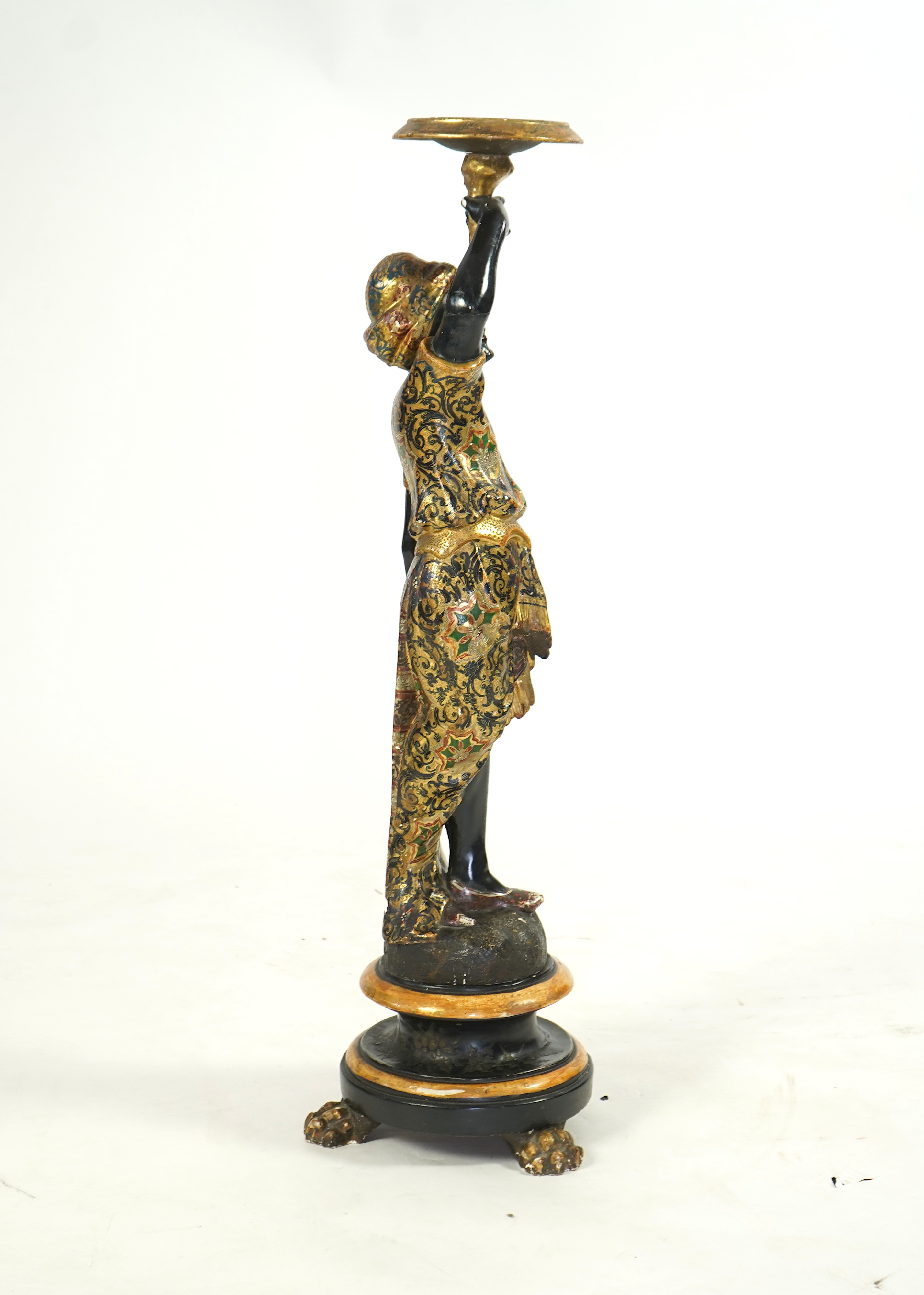 A 19th century Italian carved wood and composition polychrome painted blackamoor torchere, modelled standing with one arm holding a scroll pillar on waisted circular base and lions paw feet, 106cm high